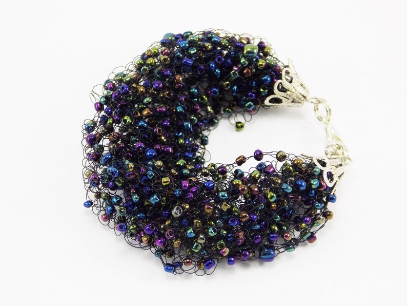 May include: A black crocheted bracelet with iridescent beads. The bracelet has silver metal clasps.