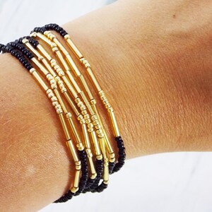 May include: A bracelet made of black and gold beads. The bracelet is layered with multiple strands of beads, creating a textured and stylish look.