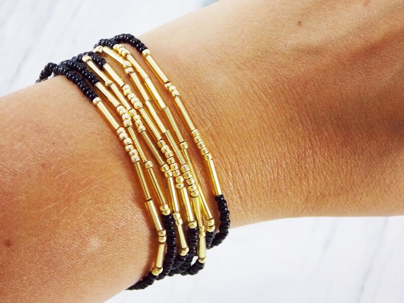 May include: A bracelet made of black and gold beads. The bracelet is layered with multiple strands of beads, creating a textured and stylish look.