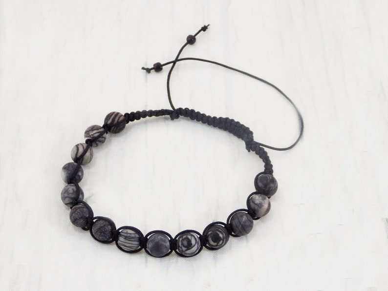 Puede incluir: Un brazalete de cord&oacute;n trenzado negro con cuentas de patr&oacute;n blanco y negro.