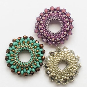 Op de afbeelding: Drie kralenringen in verschillende kleuren en patronen. De ring links is teal en goud, de ring in het midden is paars en wit, en de ring rechts is crème en zilver.