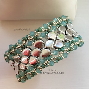 May include: A silver and turquoise beaded bracelet with the text "RAIN DROPS" and "JO BARCLAY LOGGIE © 2019".
