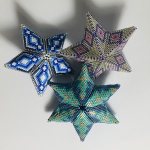 May include: Three beaded star ornaments in shades of blue, teal, silver, and purple. The stars are 3D and have a geometric pattern.
