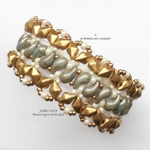 May include: Gold and gray beaded bracelet with a geometric design. The bracelet is labeled "Juno Cuff Roman Queen of the Gods".