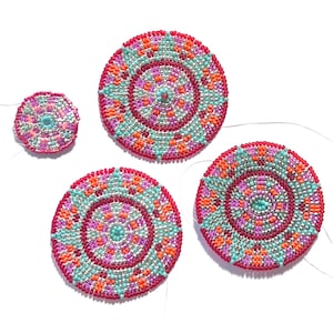 Op de afbeelding: Vier ronde kralenversieringen met een mandala-ontwerp in tinten roze, rood, oranje, turquoise en zilver. De versieringen zijn van verschillende grootte en zijn gerangschikt op een wit oppervlak.