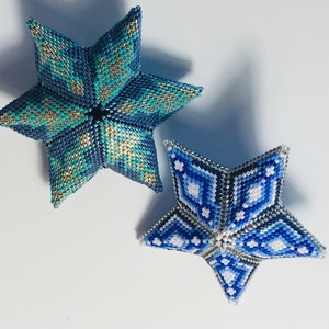 May include: Two beaded star ornaments, one blue and silver with a geometric pattern, and the other white and blue with a snowflake pattern.