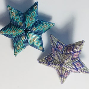 May include: Two beaded star ornaments, one blue and silver with a geometric pattern, the other silver with a purple and pink floral pattern.
