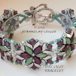 Peut inclure: Un bracelet de perles avec un motif floral. Il présente des composants métalliques argentés, des perles vertes et violettes, et des cristaux transparents. Le texte "Day Lilly Bracelet" est visible.