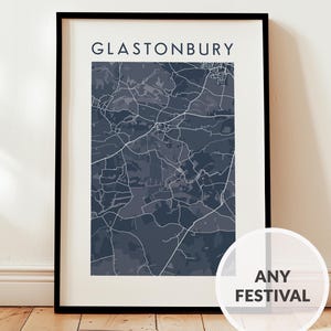 May include: A framed print of Glastonbury, Somerset, showing a detailed map in shades of grey and blue. The word "Glastonbury" is printed at the top. The print is displayed on a wooden floor.