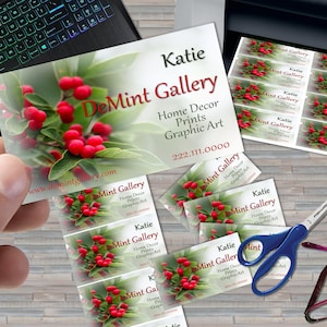 May include: A stack of business cards with a red berry and green leaf design. The text on the cards reads "DeMint Gallery", "Home Decor Prints Graphic Art", "Katie", and "222.111.0000".