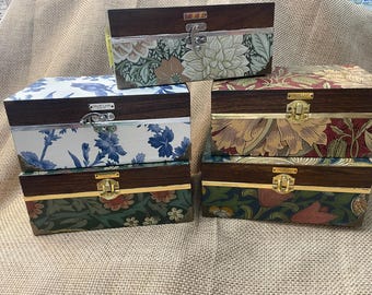 May include: Four rectangular wooden storage boxes with hinged lids and metal latches. Each box features a dark wood top section and a lower section decorated with various floral and botanical patterns in blue, green, red, and cream colors.
