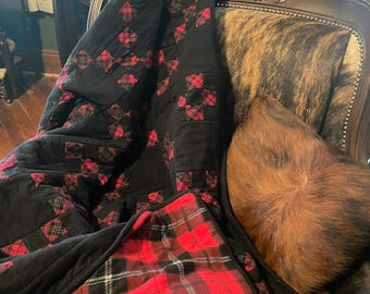 May include: A quilt featuring a patchwork design of solid black fabric squares alternating with red, black, and white plaid fabric squares. The underside of the quilt is visible, revealing a bold red, black, and white plaid pattern throughout.