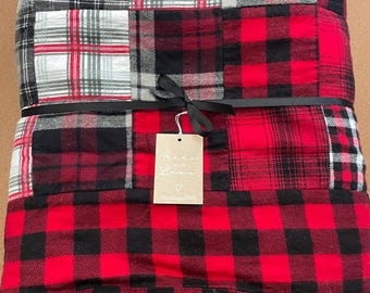 May include: A folded patchwork blanket featuring various red, black, white, and gray plaid patterns. A black ribbon is tied around the center, holding a rectangular beige tag that reads Made with Love, a heart symbol, and ChloeLane2000.