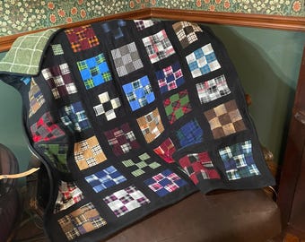 May include: A patchwork quilt constructed from various plaid and checkered fabric squares in shades of blue, red, green, brown, and white. The squares are separated by black fabric borders, and the quilt features a green plaid backing fabric.