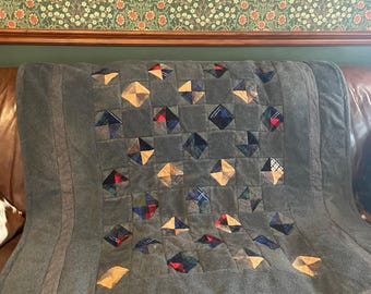 May include: A quilt featuring a central panel of dark gray fabric squares interspersed with smaller, diamond-shaped patches in various plaid and checkered patterns of red, blue, yellow, and black. The quilt has a wide, solid dark gray border.