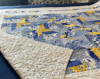 May include: A quilted bedspread featuring a patchwork design of blue, white, and yellow fabric squares. The pattern includes star motifs and various floral and geometric prints. The underside of the quilt is white with a subtle blue floral pattern.
