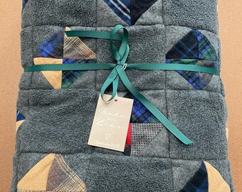 May include: A folded grey fleece blanket featuring a patchwork design of square blocks with blue, green, and tan plaid fabric accents. The blanket is tied with a dark green ribbon and includes a beige tag with the text Made with Love and ChloeLane2000.