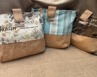 May include: Three crossbody bags with cork leather bases and fabric tops. The left bag is cream with black script and floral patterns. The center bag features vertical teal and white stripes. The right bag is brown with white cursive text.