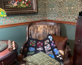 May include: A patchwork quilt featuring a grid of various plaid fabric squares in shades of red, blue, green, and black, with a solid black border and a folded section revealing an olive green fabric with a white grid pattern on the underside.