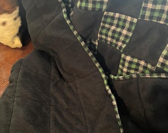 May include: A patchwork blanket featuring alternating squares of solid black fabric and a green, black, and white buffalo plaid pattern. The blanket is constructed with visible stitching between the squares and has a green plaid fabric border.