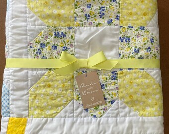 May include: A folded quilt featuring a patchwork design with white, yellow, and blue floral fabric patterns. A bright yellow ribbon is tied around the centre, holding a brown rectangular tag that reads Made with Love and Chloelane2000.