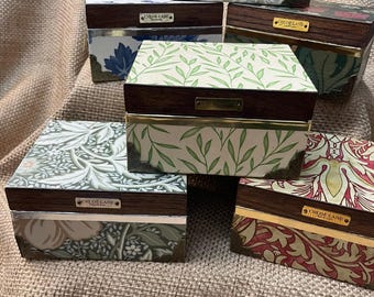 May include: A collection of six rectangular wooden boxes with hinged lids, each featuring a unique floral or botanical patterned panel, metallic corner accents, and a small rectangular metal plaque labeled Chloe Lane.