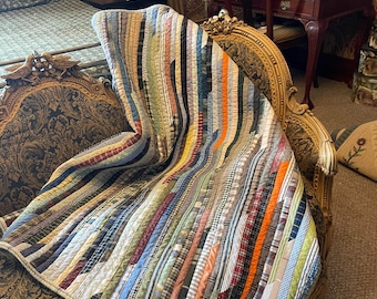 May include: A quilt constructed from numerous vertical fabric strips in a variety of colors and patterns, including plaid, striped, and solid textures. The textile features a multi-colored design with visible stitching lines separating each fabric piece.