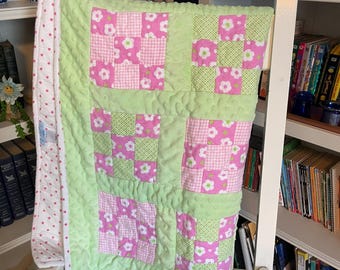 May include: A patchwork quilt featuring alternating squares of pink floral fabric, pink gingham, and light green checkered fabric, separated by a textured light green minky fabric. The quilt has a white border with small pink polka dots.