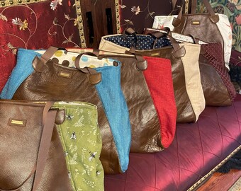 May include: A collection of five tote bags featuring brown textured panels combined with various fabric side panels, including green with bee prints, blue, red, beige, and floral patterns. Each bag has brown shoulder straps and a small rectangular logo tag.