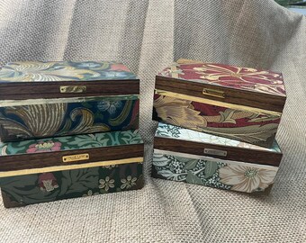 Puede incluir: Cuatro cajas rectangulares de madera con tapas abatibles, cada una con un patrón floral único en tonos azul, rojo, verde y crema. Cada caja tiene una placa de metal dorado en la tapa frontal con el texto grabado Chloe Lane.