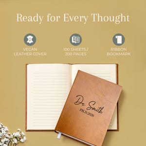 May include: A tan vegan leather notebook with the text Dr. Smith PH.D.2026 engraved on the cover. The notebook is open to reveal lined pages and includes a ribbon bookmark. The text Ready for Every Thought is displayed above the notebook.