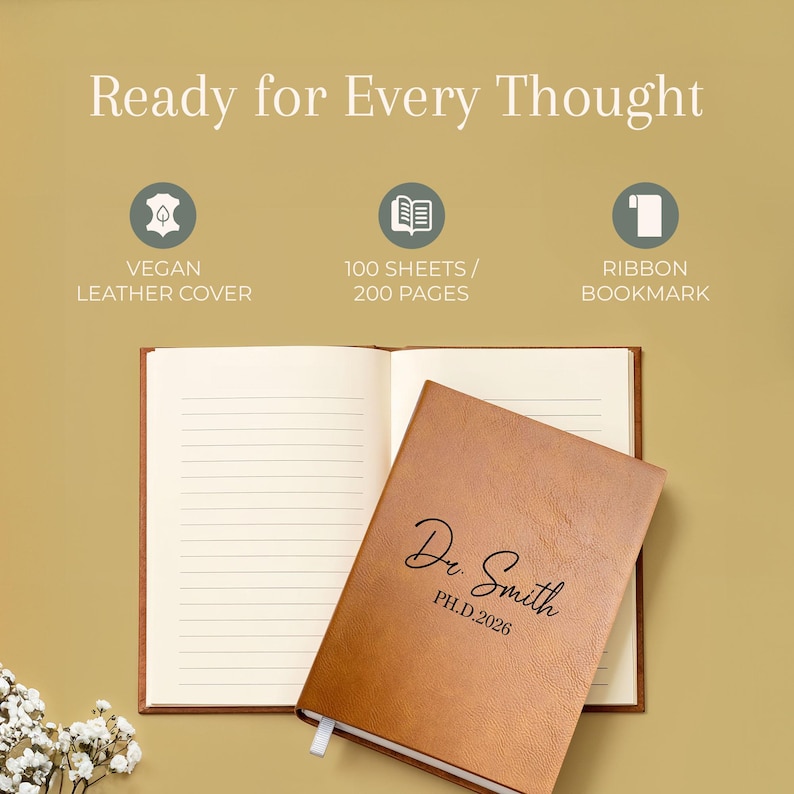 May include: A tan vegan leather notebook with the text Dr. Smith PH.D.2026 engraved on the cover. The notebook is open to reveal lined pages and includes a ribbon bookmark. The text Ready for Every Thought is displayed above the notebook.