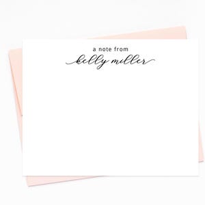 May include: A white stationery card with the text "a note from kelly miller" in black script, resting on a light pink envelope. The card is blank, offering space for a personalized message. The design is simple and elegant.