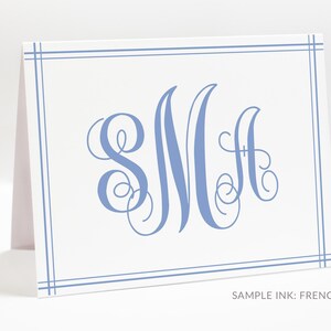 May include: A white folded note card featuring a light blue double-line border and a large, ornate, calligraphic monogram of the letters SMA in the center. The text "SAMPLE INK: FRENCH" is printed in small, simple sans-serif font at the bottom right.