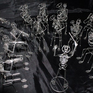 May include: A group of wire skeletons playing musical instruments. The skeletons are arranged in a band formation and are playing a variety of instruments, including a trumpet, a trombone, a tuba, and a drum. The skeletons are all made of wire and are very detailed.