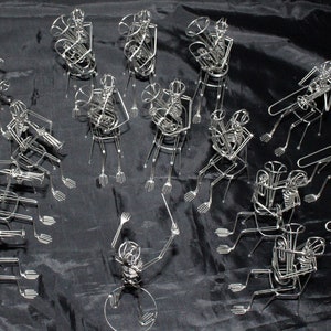 May include: A group of 15 silver wire sculptures of musicians playing instruments. The musicians are arranged in a semi-circle and are all playing different instruments, including a tuba, trumpet, trombone, and drums. The sculptures are very detailed and lifelike.