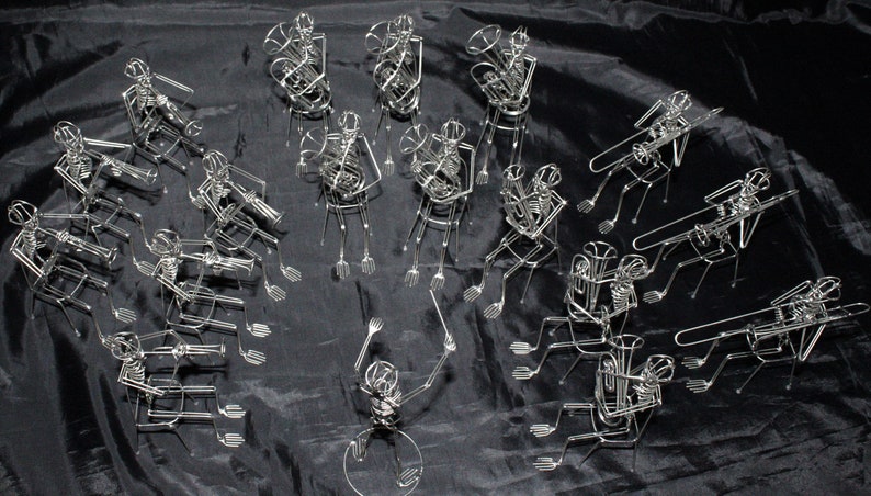 May include: A group of 15 silver wire sculptures of musicians playing instruments. The musicians are arranged in a semi-circle and are all playing different instruments, including a tuba, trumpet, trombone, and drums. The sculptures are very detailed and lifelike.