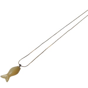 May include: A gold-colored necklace with a fish-shaped pendant. The pendant is a light yellow color and has a smooth, polished appearance. The chain is thin and delicate, and the clasp is small and simple.