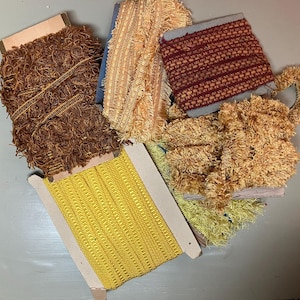 Könnte beinhalten: Eine Sammlung von dekorativen Zierbandrollen in verschiedenen Farben. Die Bänder umfassen braune, gelbe und beige Fransen sowie eine gelbe Webkante und eine rot-beige gemusterte Kante. Die Rollen sind aus Pappe.