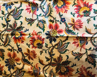 May include: A cream-colored fabric with a floral pattern. The flowers are red, yellow, and blue, and the leaves are green and brown.
