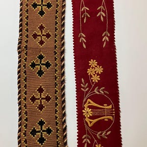 May include: Two fabric trims, one with a brown background and a repeating pattern of black crosses, the other with a red background and gold embroidered flowers and a lyre.
