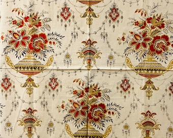 Puede incluir: Tela de color crema con un patrón repetido de arreglos florales en jarrones ornamentados. Las flores son rojas y doradas, con detalles en negro. El diseño incluye cadenas decorativas y elementos colgantes.