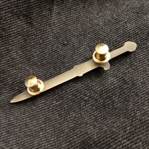 Pu&ograve; includere: Uno spillo a forma di spada in metallo dorato con due dorsi rotondi in metallo dorato.