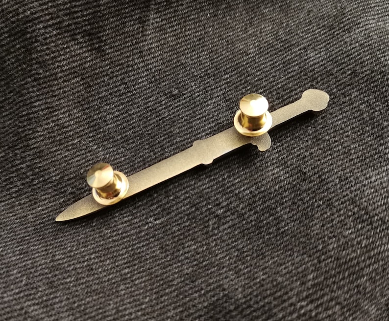 Pu&ograve; includere: Uno spillo a forma di spada in metallo dorato con due dorsi rotondi in metallo dorato.