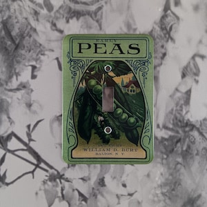 May include: A green and white light switch cover with a vintage illustration of peas. The text reads "Early Peas Put Up By William D. Burt Dalton, N.Y."