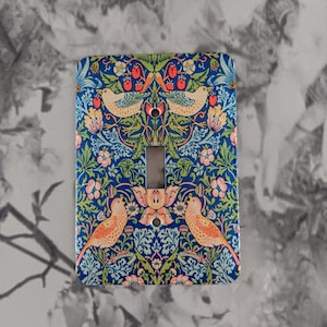 May include: A light switch cover with a blue background and a floral pattern featuring birds and strawberries. The pattern is reminiscent of William Morris's designs.