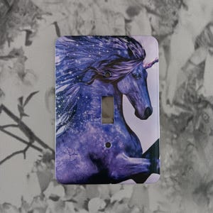 May include: A light switch cover featuring a purple and blue unicorn with a starry background. The unicorn is running with its mane flowing in the wind.
