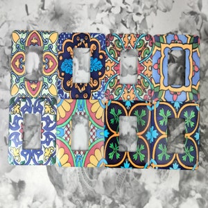 May include: Eight colourful light switch covers with intricate tile patterns in shades of blue, green, red, yellow, and black. The covers have a rectangular shape with a cut-out for a light switch.