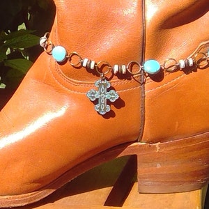 May include: Brown leather cowboy boot with a turquoise and white beaded ankle bracelet with a silver cross charm.