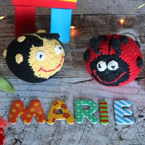 May include: A wooden block tower with a red, yellow, and blue color scheme.  The tower is next to a knitted bee and ladybug toy.  The word "MARIE" is spelled out with colorful letters.